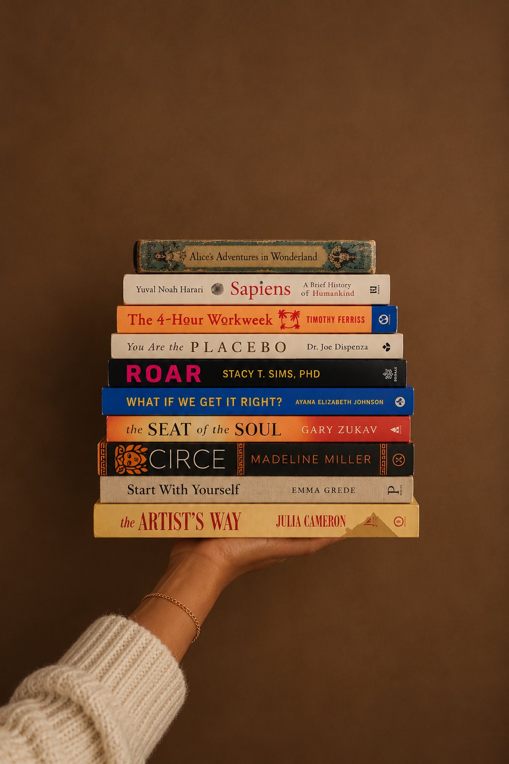 A hand holding a stack of favorite books — Alice's Adventures in Wonderland, Sapiens, The 4-Hour Workweek, You Are the Placebo, Roar, Circe, The Artist's Way and more