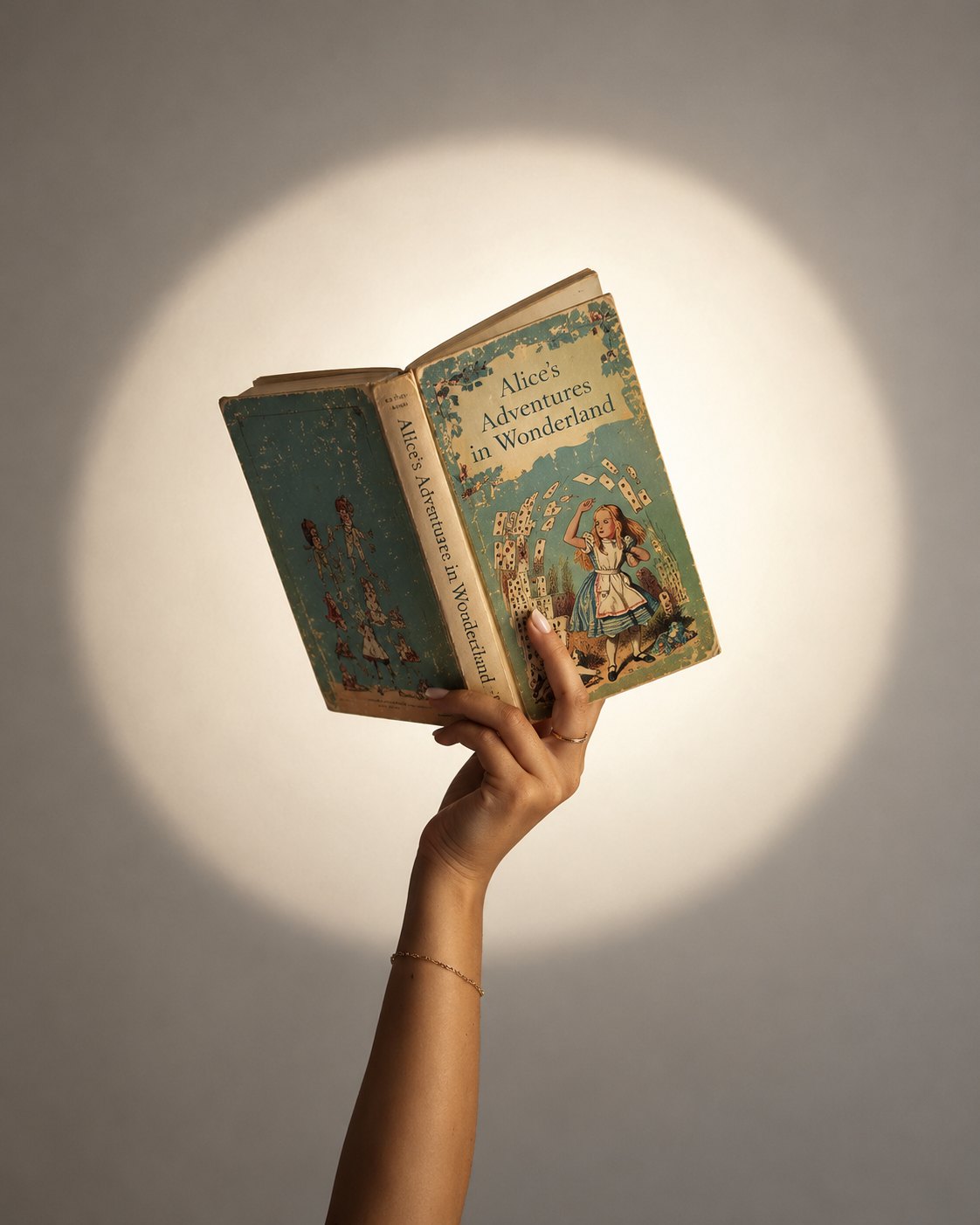 A hand holding up a vintage copy of Alice's Adventures in Wonderland in a circle of warm light
