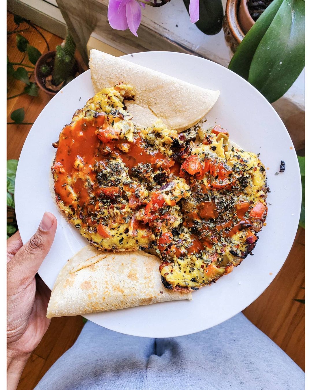 vegan eggless omelet with tomatoes, hot sauce, bell peppers, oregano, and tortillas on the side.