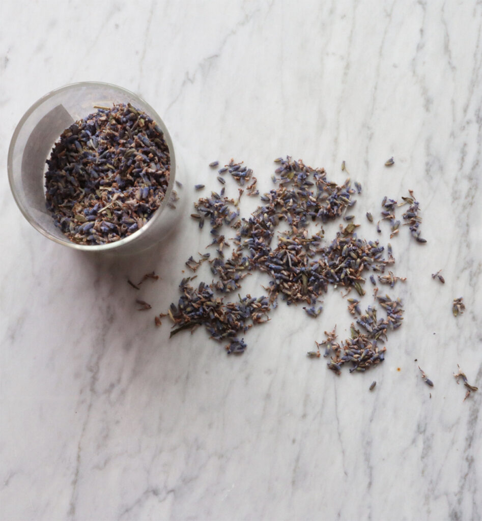 Lavender buds in an open glass jar and outside of jar. 