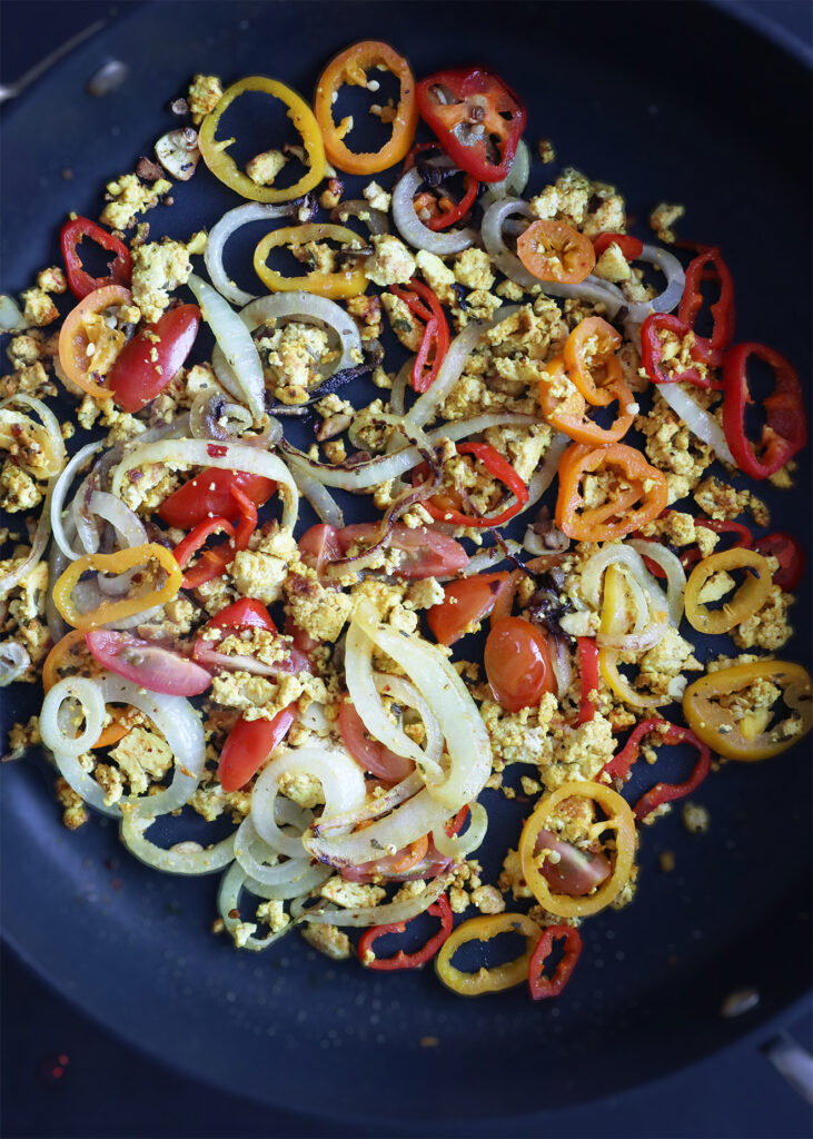 scrambled tofu on a skillet with onions, bell peppers, and garlic. 