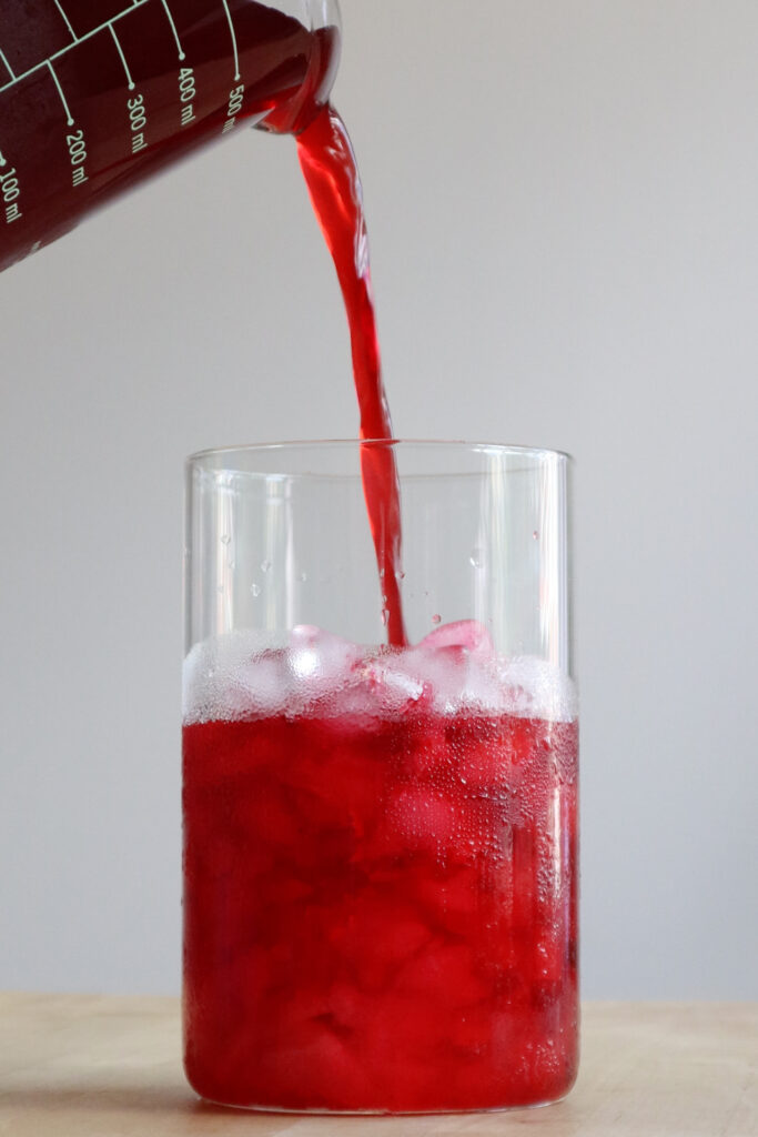 Pouring hibiscus agua fresca, into a glass cup with ice